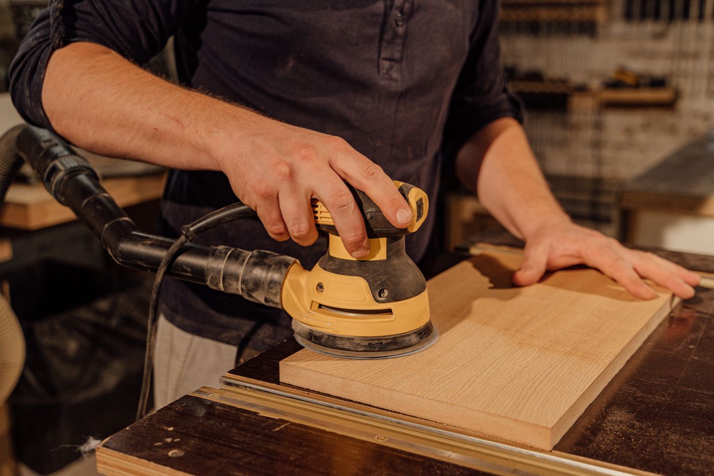 Hands sanding a timber board with an orbital sander