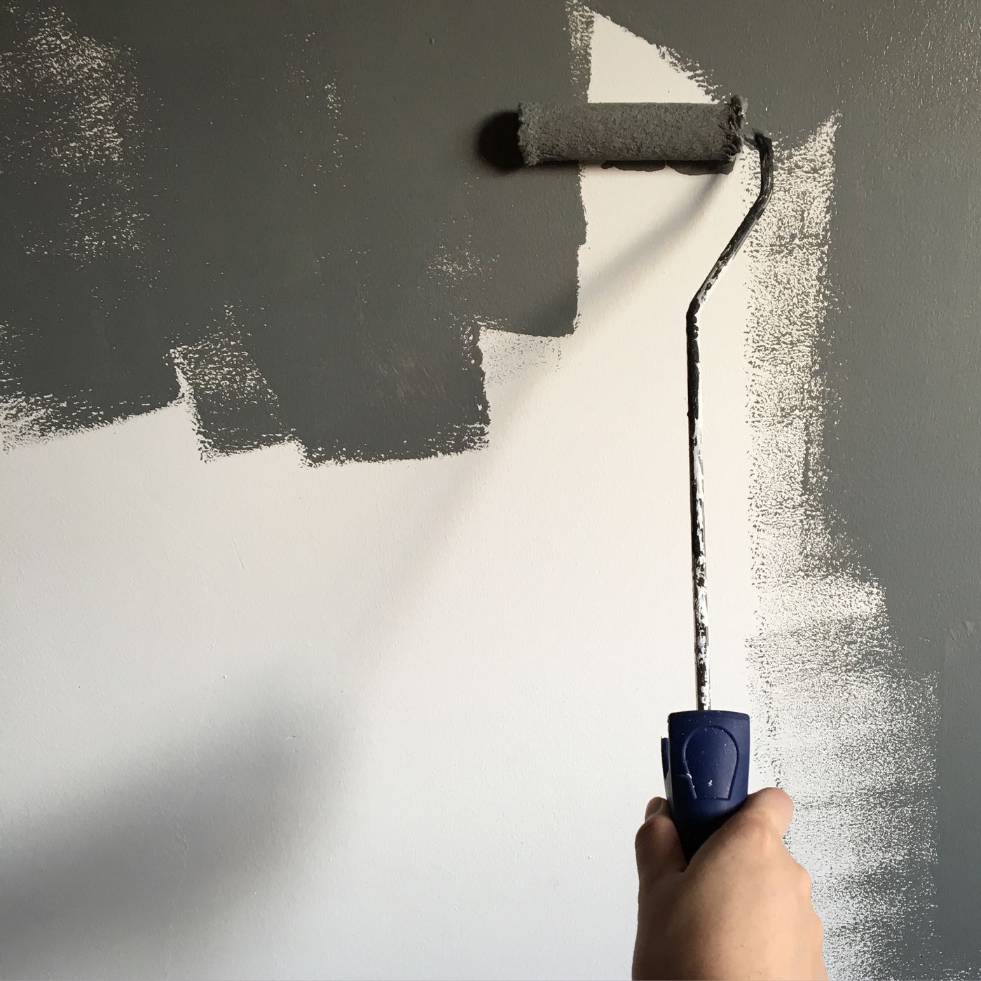 Paint roller applying grey paint to a partly painted wall